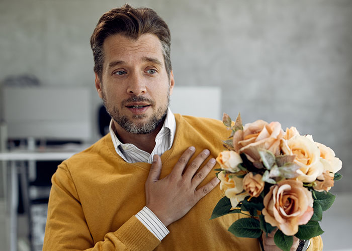 Man in a yellow sweater holding flowers, gestures with hand on chest, symbolizing questions about men.