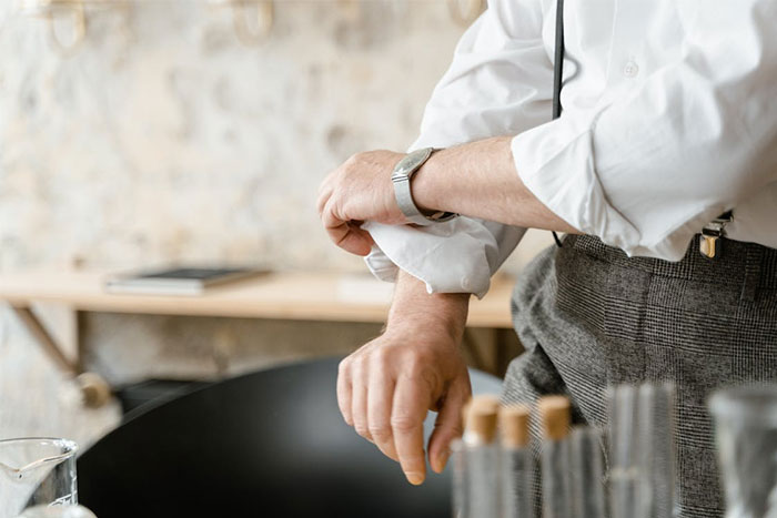 Man adjusting his shirt sleeves, standing near a table, focusing on daily tasks with attention to detail.
