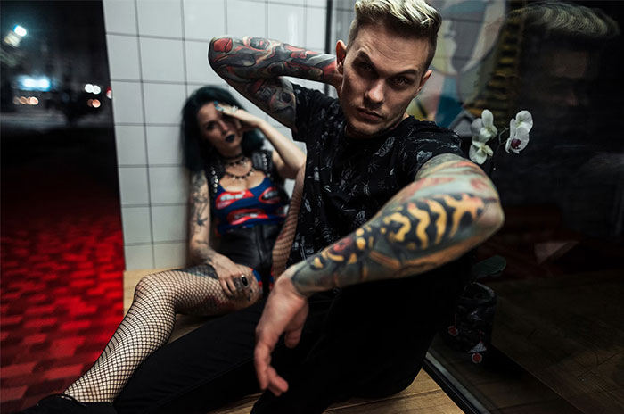 Tattooed man and woman in edgy outfits, posing indoors, representing men's curiosity about asking women embarrassing questions.