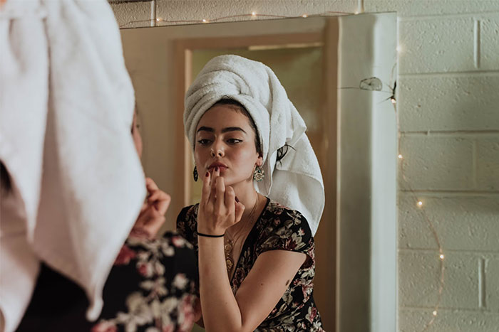 Woman with a towel on her head applying lipstick, reflecting in a mirror, related to questions men find embarrassing.