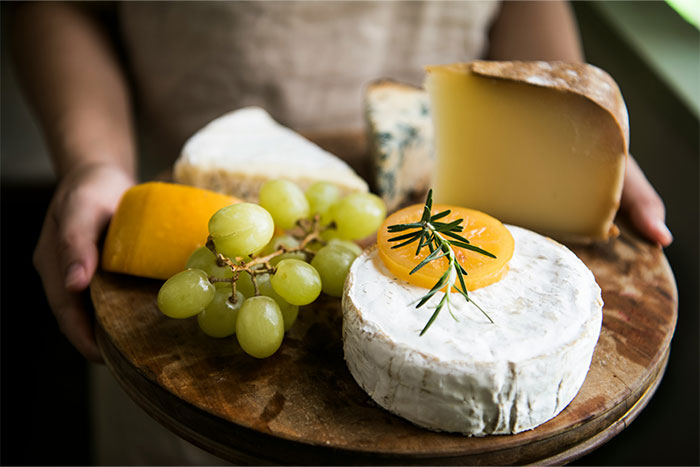 A wooden platter with assorted cheeses, grapes, and rosemary garnish, presented as an elegant appetizer.