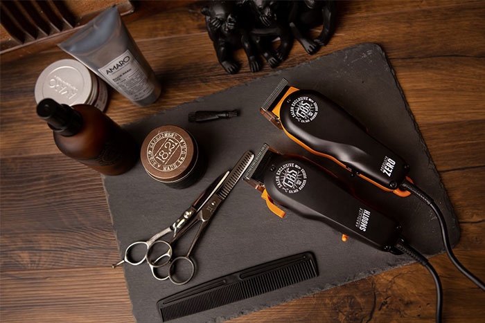 Men's grooming tools and products on a wooden table, including clippers, scissors, and styling cream.