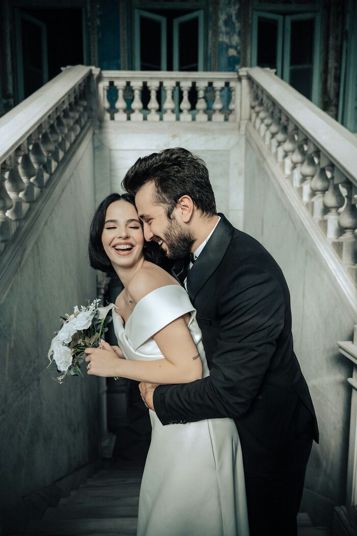 Bride and groom embracing on a staircase, holding a bouquet, smiling warmly at their wedding.