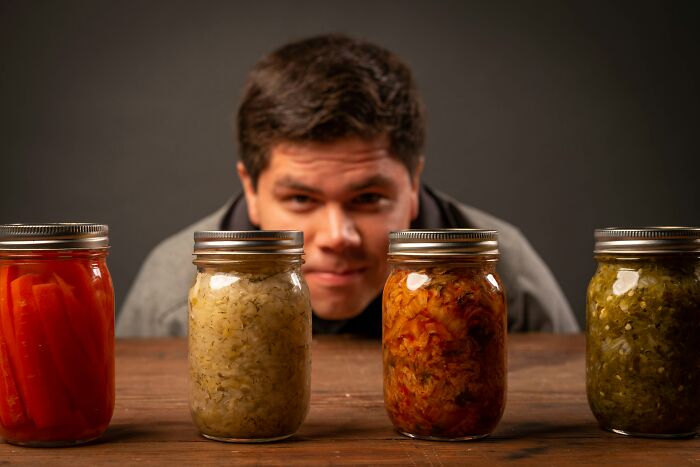 A person looking at four jars of pickled vegetables on a table, illustrating simple lifestyle approaches.