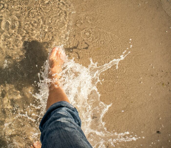 A barefoot person splashing through shallow water on a sandy beach.