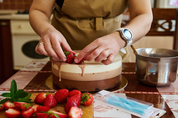 Hands decorating a cake with strawberries, highlighting job misconceptions in baking.