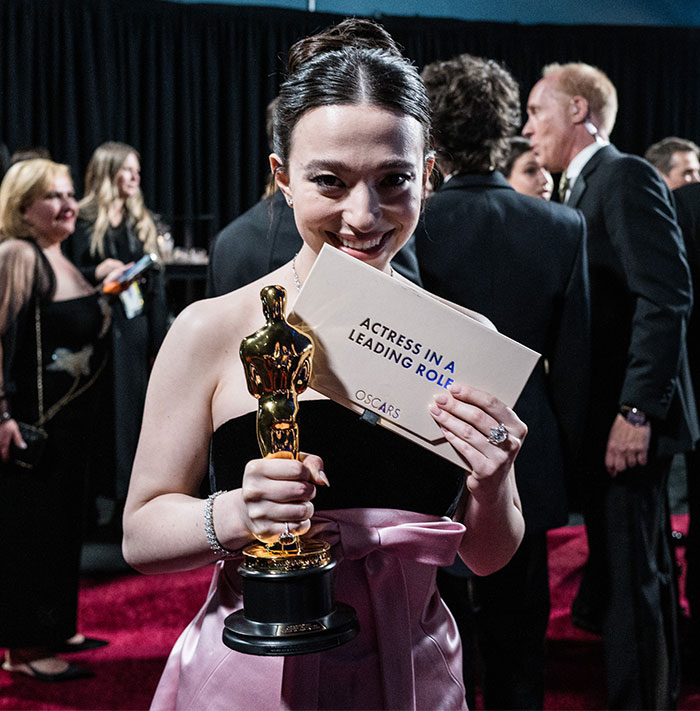 Smiling woman holding Oscar and winner's envelope backstage at Oscars 2025.