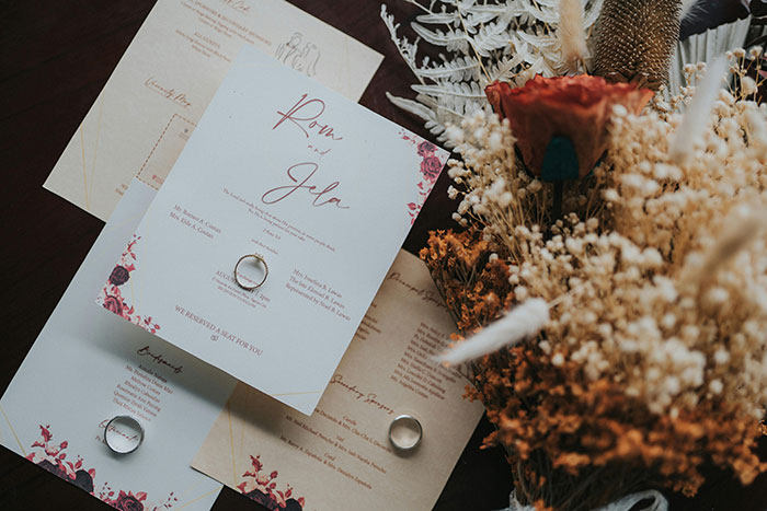 Wedding invitations with elegant design and rings, surrounded by dried flowers, reflecting mil-expectations style.