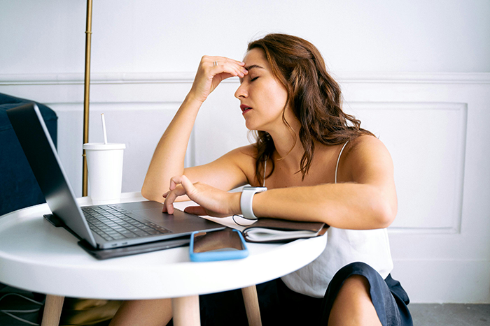 Woman stressed at a table with a laptop, planning wedding invitations and expectations.