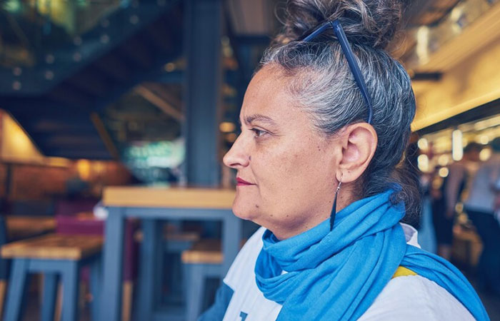 Woman with blue scarf sitting at a table, highlighting cultural dynamics in cooking between Chinese DIL and MIL. Woman with blue scarf sitting at a table, highlighting cultural dynamics in cooking between Chinese DIL and MIL.