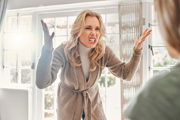 A woman in a beige cardigan expresses anger in a bright room, gesturing with her hands; toxic MIL context suggested. A woman in a beige cardigan expresses anger in a bright room, gesturing with her hands; toxic MIL context suggested.