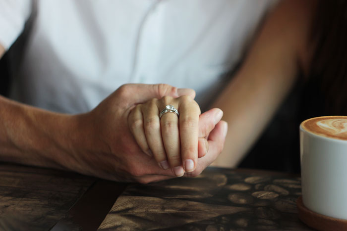 Hands holding, featuring a wedding ring, with coffee on table, symbolizing family tension over heirloom jewelry. Hands holding, featuring a wedding ring, with coffee on table, symbolizing family tension over heirloom jewelry.