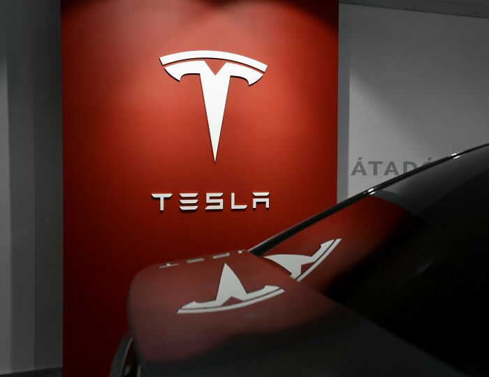 Tesla logo on a red wall with a car reflection, linking to European news stories.