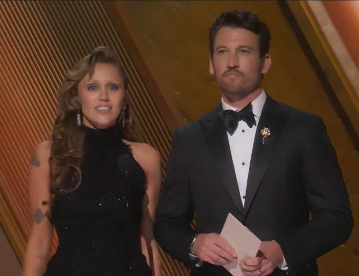 Miley Cyrus and Miles Teller on stage at the Oscars, dressed in formal attire.