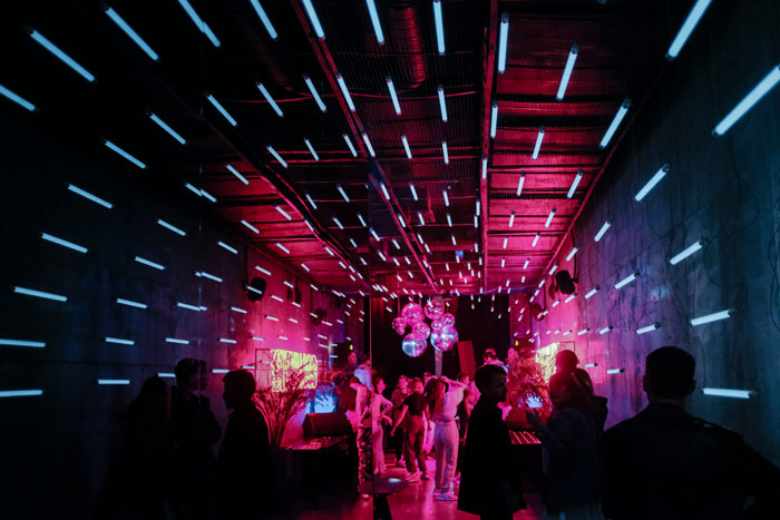 People socializing at a vibrant party with neon lights, linked to model's case and possible trafficking investigation activities.