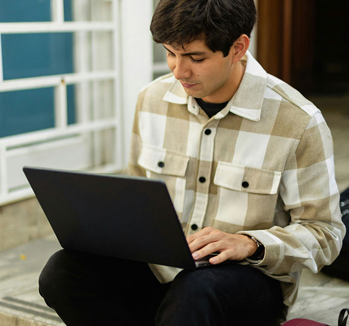Man using a laptop outdoors, wearing a plaid shirt, representing modern conveniences.