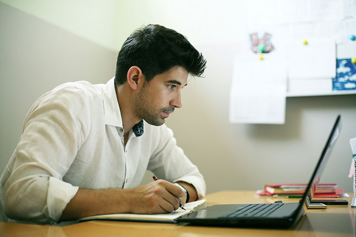 Man in white shirt at laptop taking notes, highlighting modern conveniences.