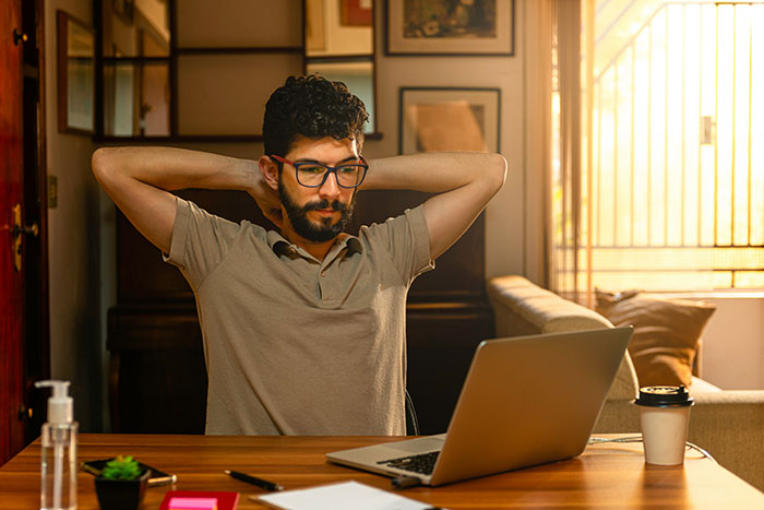 Man with glasses stretches at a table, showing frustration with modern conveniences while using a laptop in a cozy room.