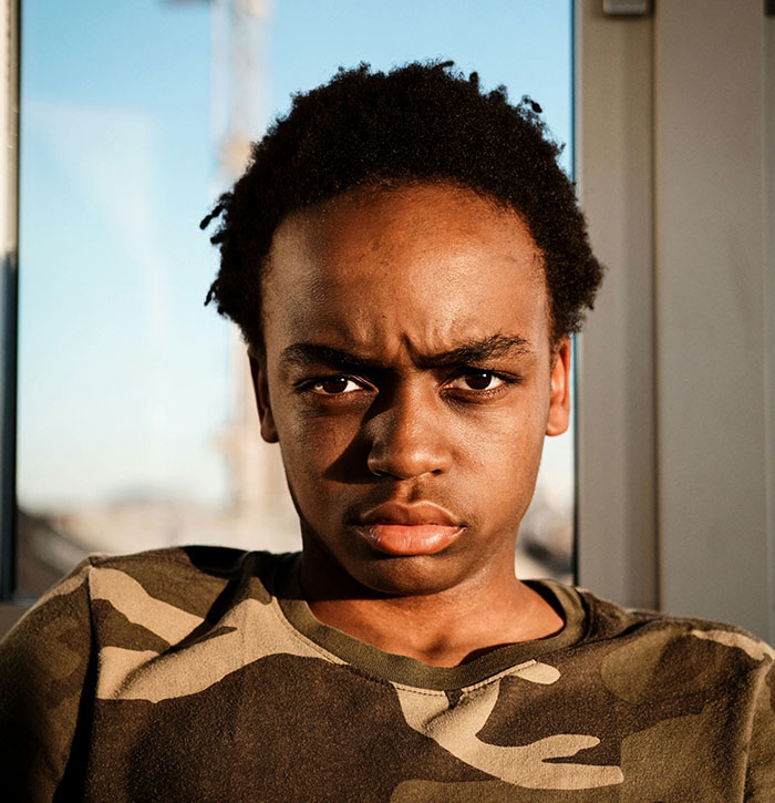 Person in a camo shirt by a window, looking displeased with modern conveniences.