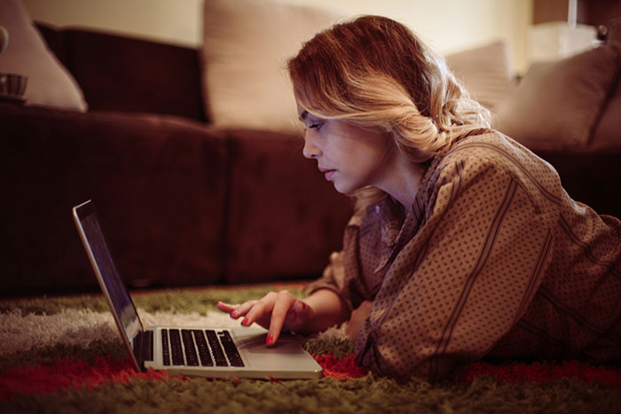 Woman lying on a rug using a laptop, illustrating modern convenience.