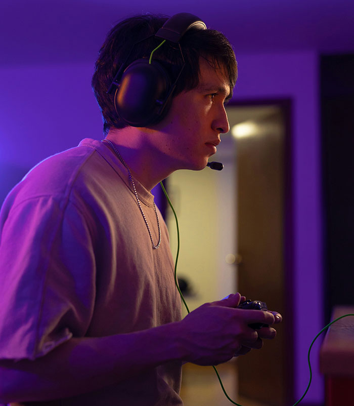 Person gaming with headphones and controller, illuminated by purple light, highlighting modern convenience.