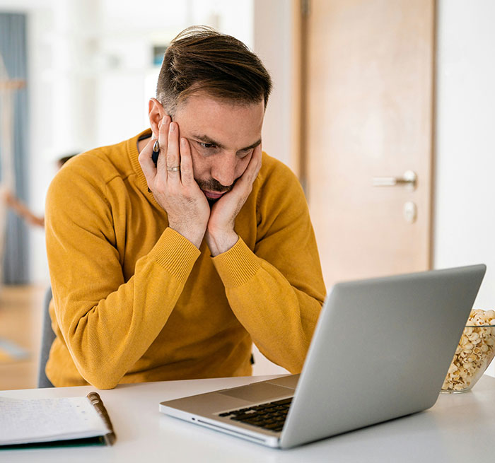 Man in a mustard sweater looking frustrated at a laptop, surrounded by modern conveniences.