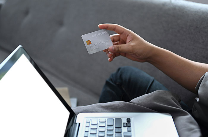 Person holding credit card near laptop, illustrating modern conveniences.