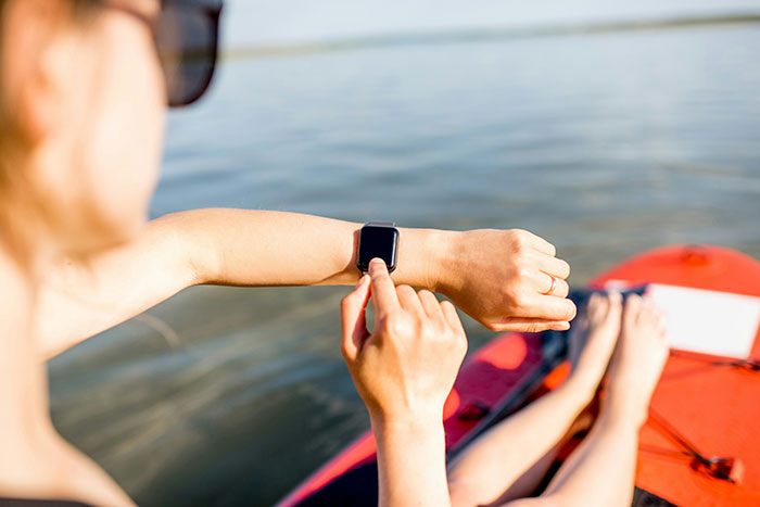 Person using a smartwatch on a kayak, demonstrating modern conveniences while enjoying a relaxing activity on the water.