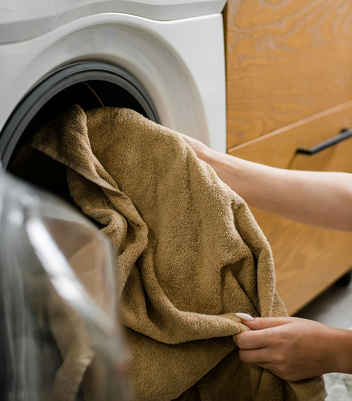Person loading a brown towel into a washing machine, representing a modern convenience that some find bothersome.