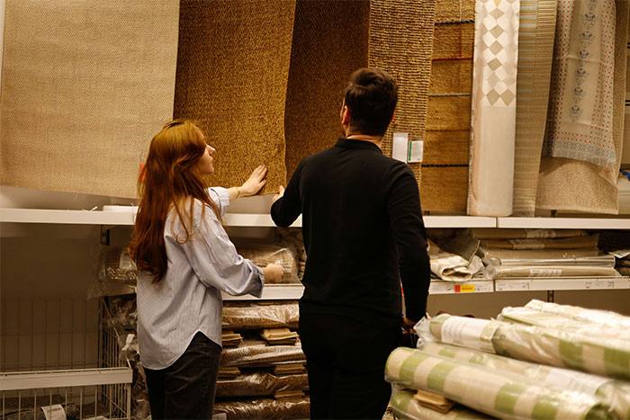 Two people examining carpet rolls in a store, discussing the industry as a potential ripoff.