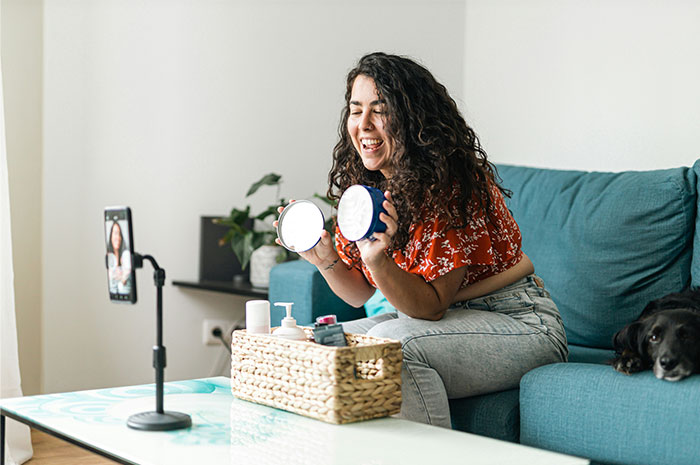 Woman filming a skincare review on a sofa, engaging with viewers about industry insights with beauty products on the table.