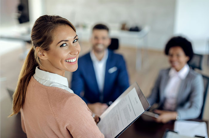 Person smiling at the camera holding a resume in a business meeting, highlighting industry ripoff realization.