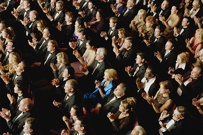 Audience in formal attire clapping, related to industry realization as a possible ripoff.
