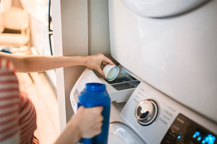 Person adding detergent to a washing machine, highlighting industry as a potential ripoff.