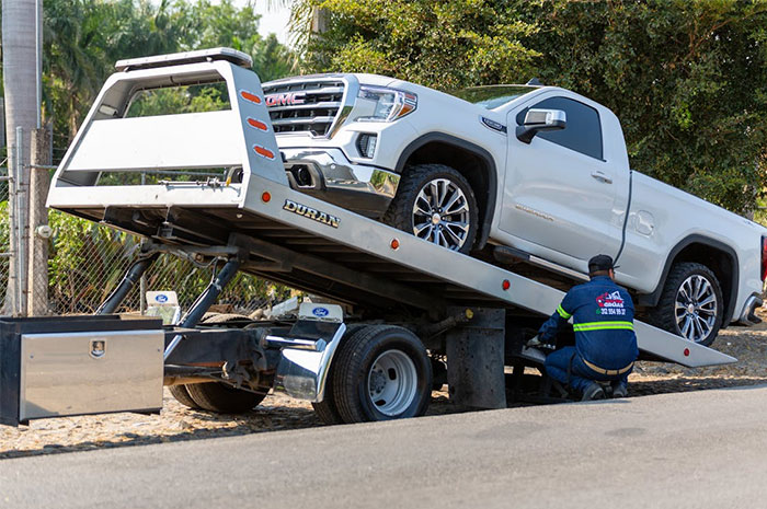 Tow truck operator loading a white GMC pickup, highlighting potential industry ripoff insights.