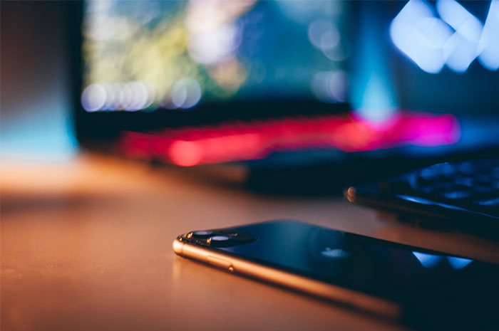 A smartphone on a desk with a laptop in the background, evoking thoughts on industry ripoffs.