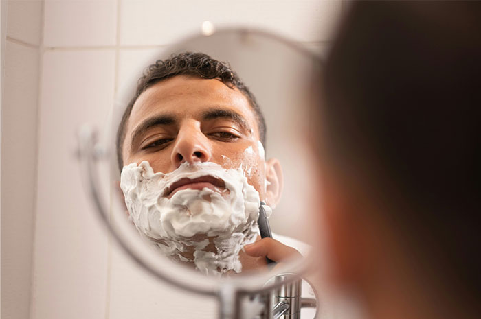 Man shaving in front of a mirror, highlighting ripoff concerns in grooming industry.