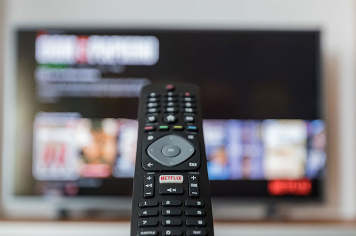 Remote control pointed at a TV displaying Netflix, hinting at the industry's perceived ripoff.