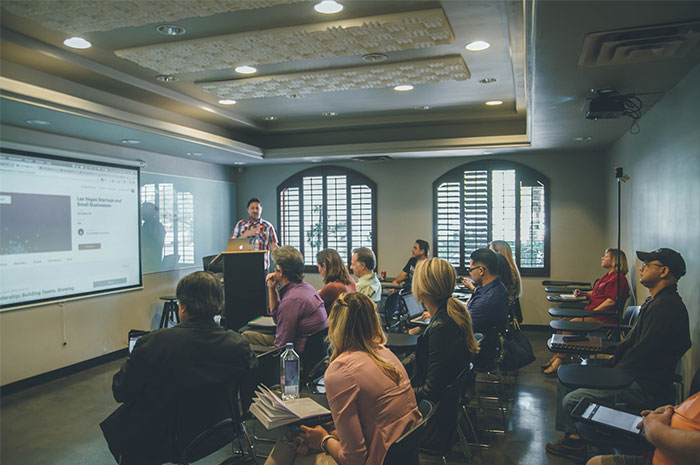 Audience in a conference room listening to a presentation about industry ripoffs.