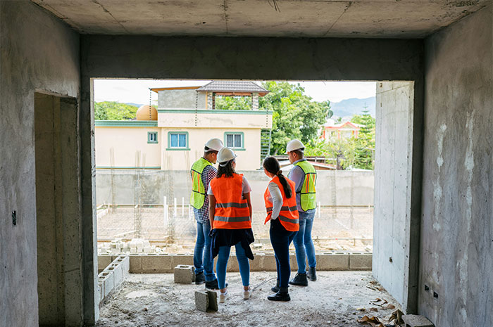 Construction workers in vests and helmets, assessing a building site with an industry critique in mind.