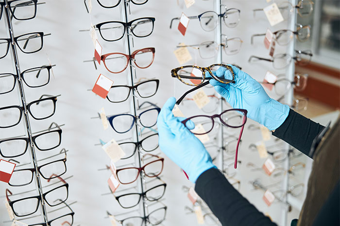 Person with gloves holds glasses in an eyewear store, illustrating industry ripoff concerns.