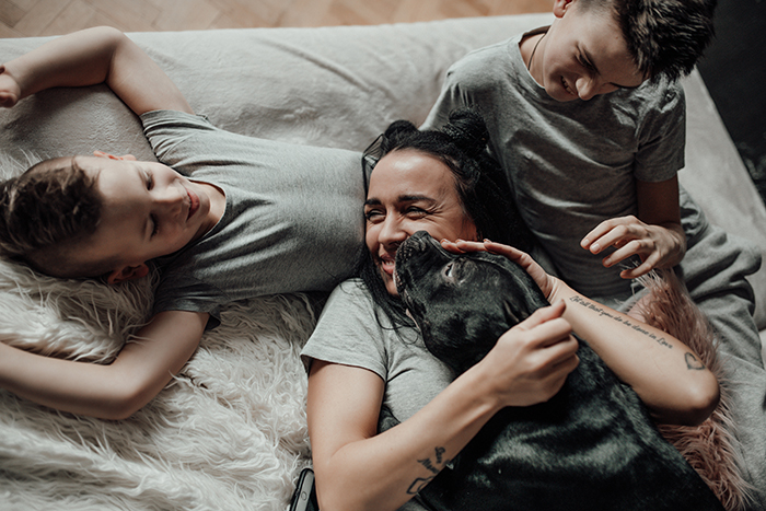 Family cuddling with a beautiful dog on the sofa, everyone smiling and wearing grey shirts.