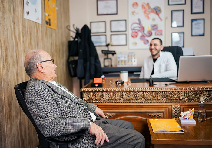 An elderly man and a smiling doctor sit in an office discussing coincidences.