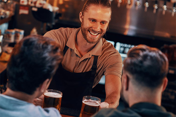 Barman serves drinks to two customers at a bar, creating a friendly atmosphere.