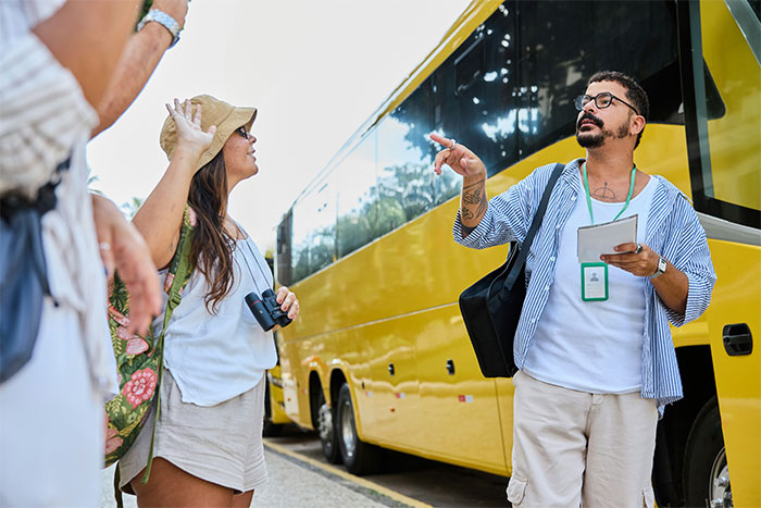 Tour guide explaining coincidences stories to tourists near yellow bus.