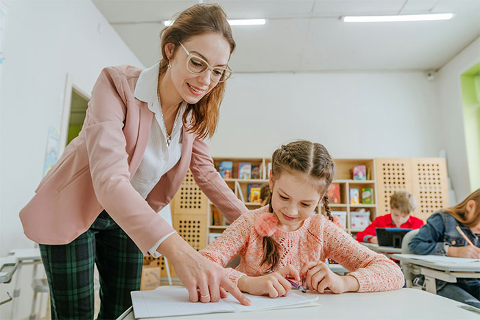 Teacher helps student with a task in the classroom, demonstrating a memorable learning moment.