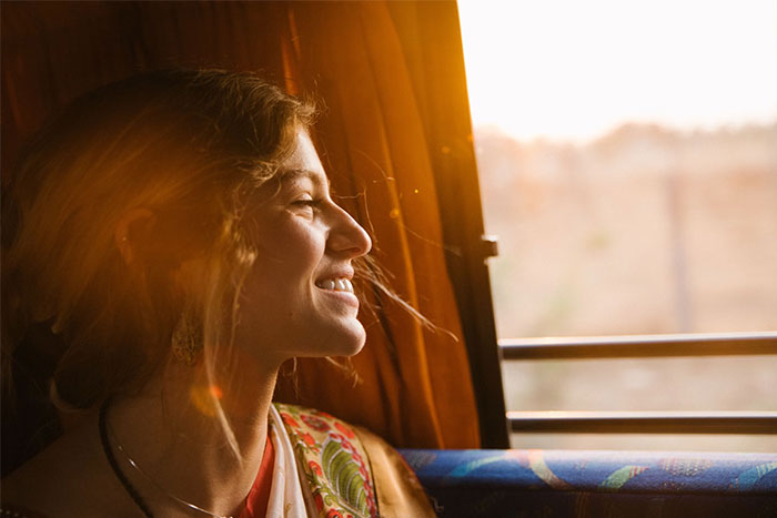 Woman smiling by a window with sunlight, capturing a moment of joy and coincidence.