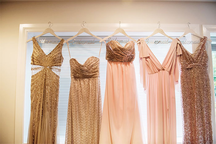 Bridesmaids' dresses in various styles and shades of pink and gold hanging on labeled hangers.