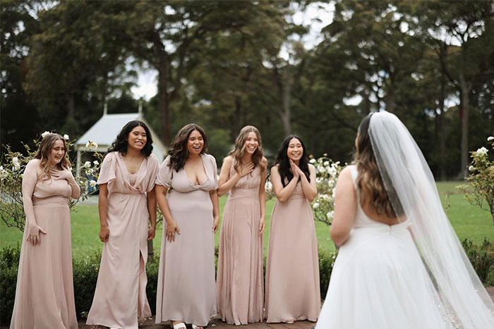 Bride and bridesmaids in pastel dresses laughing together in a garden setting.