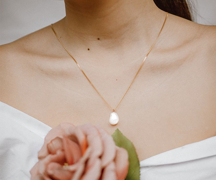 Woman in a white dress with a pearl necklace, holding a rose, illustrating bridesmaids' experiences.